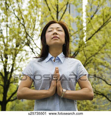 Mid-adult Asian woman standing outside with trees and skyscrapers behind her meditating. View Large Photo Image Stock Image - Mid-adult Asian woman standing outside with trees and skyscrapers behind her meditating.. Fotosearch
