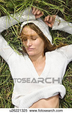 Stock Photography - Portrait of attractive young redheaded woman lying in grass resting.. Fotosearch