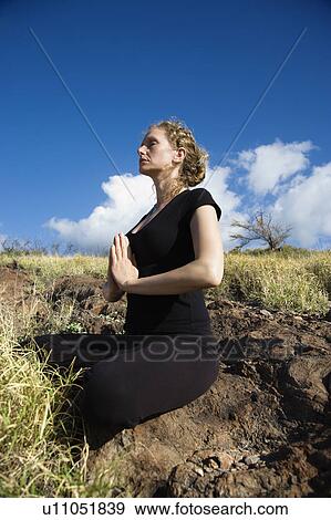 Stock Photo - Side view of a woman sitting in yoga lotus position on rocks in Maui, Hawaii. Fotosearch