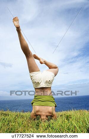 Picture - Woman doing headstand in grass near ocean. Fotosearch