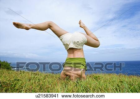 Woman doing headstand with legs askew in grass near ocean View Large Photo Image Stock Image - Woman doing headstand with legs askew in grass near ocean. Fotosearch