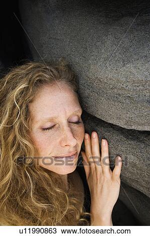 Stock Image - Woman smiling with eyes closed leaning against rock. Fotosearch