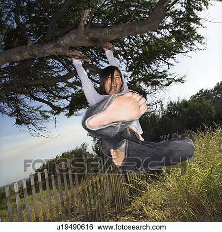 Stock Photograph - Young adult Asian female holding on to a tree and kicking towards viewer.. Fotosearch