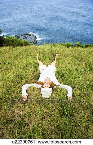 Young woman relaxing in grass near ocean in Maui, Hawaii. View Large Photo Image Stock Image - Young woman relaxing in grass near ocean in Maui, Hawaii.. Fotosearch