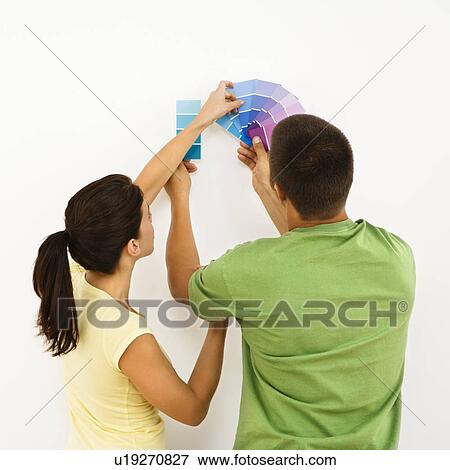 Stock Photo - Attractive young adult couple holding color paint samples up to white wall.. Fotosearch