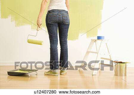 Stock Image - Back view of Caucasian woman holding paint roller with painting supplies.. Fotosearch