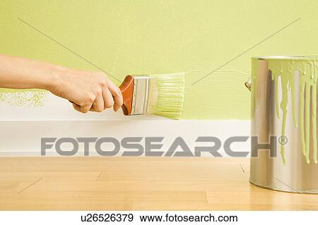 Stock Photo - Caucasian female hand painting trim on wall beside paint can.. Fotosearch