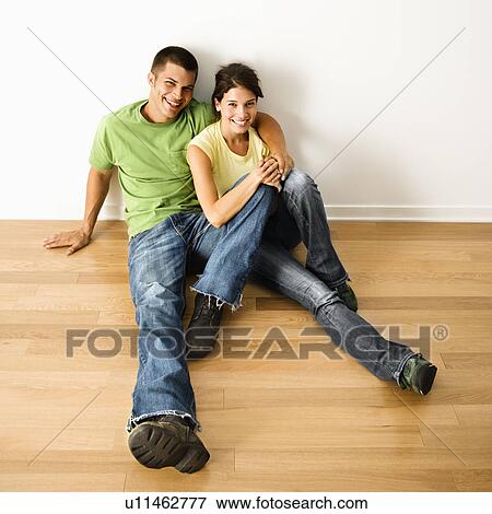 Stock Photo - Couple sitting close on hardwood floor in home smiling. Fotosearch