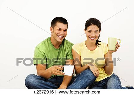 Stock Image - Couple sitting on floor drinking coffee and smiling.. Fotosearch