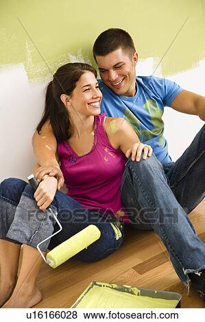 Stock Photo - Couple sitting on floor smiling taking a break from painting home. Fotosearch