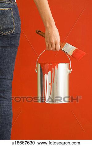 Stock Image - Female hand and leg holding paint can and paintbrush. Fotosearch