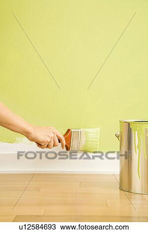 Stock Image - Hand painting trim on wall beside paint can. Fotosearch