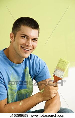 Stock Photo - Smiling man kneeling in front of partially painted wall holding paintbrush.. Fotosearch
