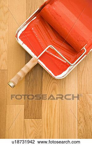 Stock Image - Still life of paint roller in tray on wood floor. Fotosearch