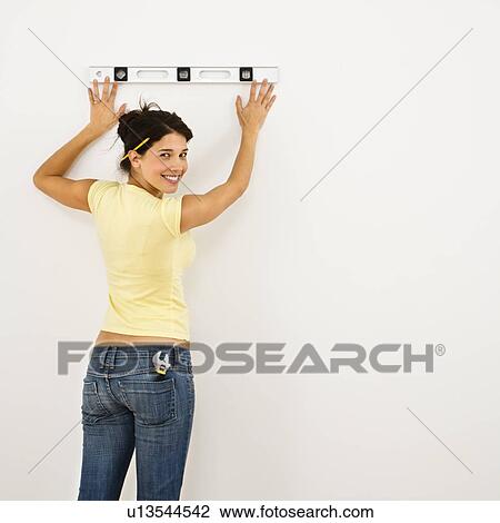 Stock Image - Woman standing holding level up to interior wall. Fotosearch