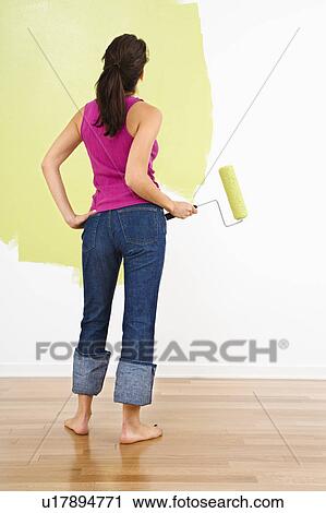 Woman standing holding paint roller admiring partially painted interior wall View Large Photo Image Stock Image - Woman standing holding paint roller admiring partially painted interior wall. Fotosearch