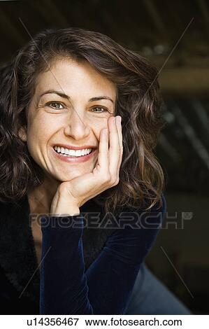 Stock Photo - Portrait of pretty mid adult Caucasian woman smiling with head on hand making eye contact.. Fotosearch