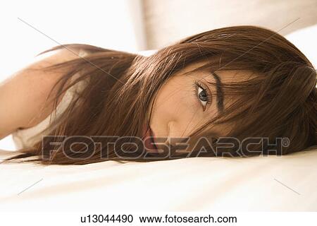 Stock Image - Pretty young Caucasian woman lying on bed making eye contact.. Fotosearch