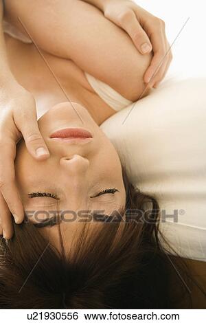Stock Photograph - Pretty young Caucasian woman lying on bed with head hanging over with eyes closed.. Fotosearch