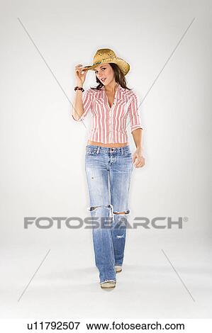 Stock Photo - Young Caucasian woman walking to viewer and tilting cowboy hat.. Fotosearch