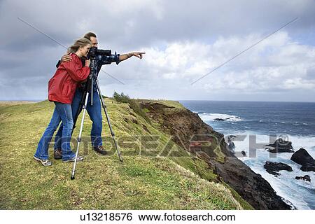 Couple looking off the coast through a camera on a tripod View Large Photo Image Stock Photograph - Couple looking off the coast through a camera on a tripod . Fotosearch