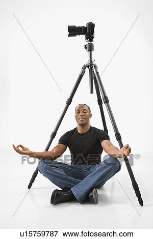 Stock Photo - Man sitting meditating under camera and tripod. Fotosearch
