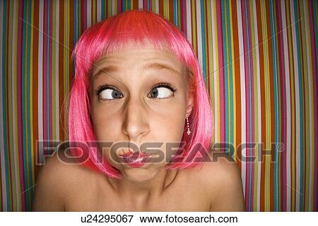 Stock Photo - Portrait of attractive young adult woman wearing pink wig against striped background making cross eyed expression.. Fotosearch