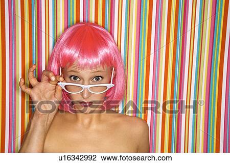 Stock Image - Woman wearing pink wig peeking over glasses . Fotosearch