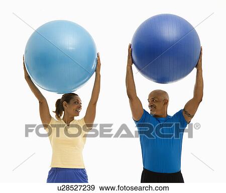 Happy smiling mid adult multiethnic man and woman holding blue exercise balls over their heads looking at each other. View Large Photo Image Stock Photo - Happy smiling mid adult multiethnic man and woman holding blue exercise balls over their heads looking at each other.. Fotosearch
