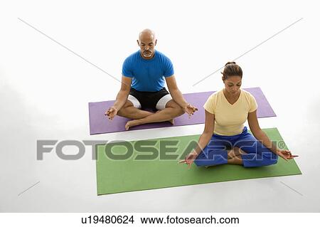 Mid adult man and woman sitting in lotus position on exercise mats with eyes closed and legs crossed. View Large Photo Image Picture - Mid adult man and woman sitting in lotus position on exercise mats with eyes closed and legs crossed.. Fotosearch