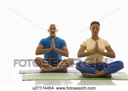 Picture - Mid adult man and woman sitting in Namaste position on exercise mats with eyes closed and hands at heart center. Fotosearch