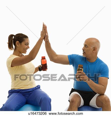 Mid adult multiethnic man and woman sitting on blue exercise balls giving each other the high five View Large Photo Image Stock Photograph - Mid adult multiethnic man and woman sitting on blue exercise balls giving each other the high five. Fotosearch