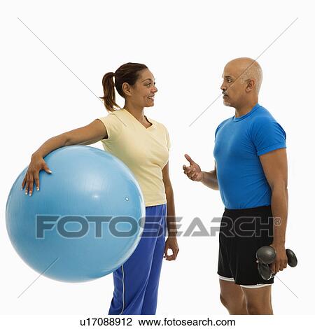 Mid adult multiethnic woman holding blue exercise ball standing with mid adult multiethnic man looking at each talking. View Large Photo Image Stock Image - Mid adult multiethnic woman holding blue exercise ball standing with mid adult multiethnic man looking at each talking.. Fotosearch