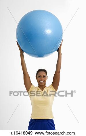 Mid adult woman standing and holding blue exercise ball over her head looking at viewer and smiling. View Large Photo Image Stock Photo - Mid adult woman standing and holding blue exercise ball over her head looking at viewer and smiling.. Fotosearch