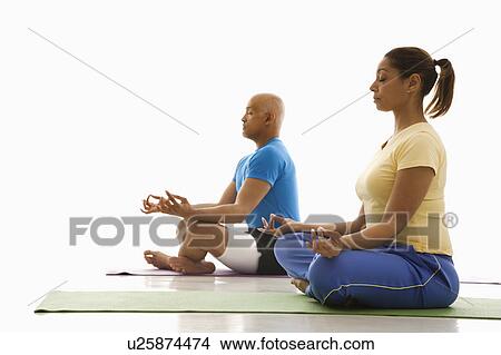 Picture - Side view of mid adult man and woman sitting in lotus position on exercise mats with eyes closed and legs crossed.. Fotosearch