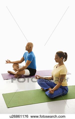 Stock Photograph - Side view of mid adult man and woman sitting in lotus position on exercise mats with eyes closed and legs crossed.. Fotosearch