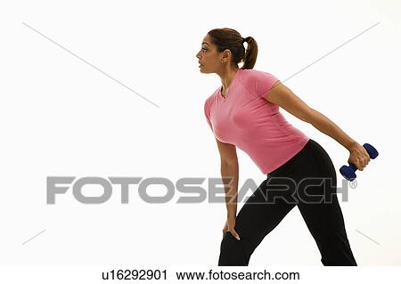 Stock Image - Side view of mid adult woman wearing pink shirt exercising with dumbbell.. Fotosearch