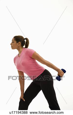 Stock Photo - Side view of mid adult woman wearing pink shirt exercising with dumbbell.. Fotosearch