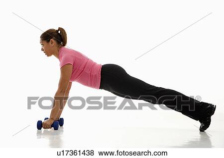 Stock Photo - Side view of mid adult woman wearing pink exercise shirt doing pushups while holding dumbbells.. Fotosearch