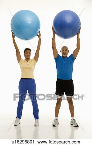 Smiling mid adult man and woman holding blue exercise balls over their heads looking at viewer. View Large Photo Image Stock Image - Smiling mid adult man and woman holding blue exercise balls over their heads looking at viewer.. Fotosearch