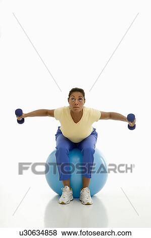 Stock Photo - Woman balancing on exercise ball holding dumbbells. Fotosearch