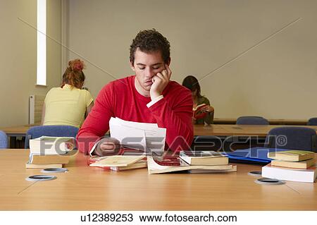 Bored young man seated at desk studying View Large Photo Image Stock Image - Bored young man seated at desk studying. Fotosearch