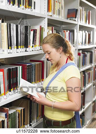 Stock Photo - Young woman reading book in library. Fotosearch