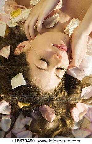 Stock Image - Above view of Caucasian mid-adult woman lying down with hair spread out on rose petals. . Fotosearch