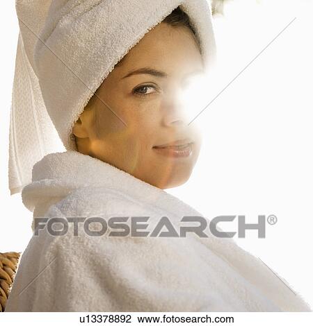 Stock Image - Caucasian mid-adult woman wearing robe and towel on head with sunlight behind her.. Fotosearch
