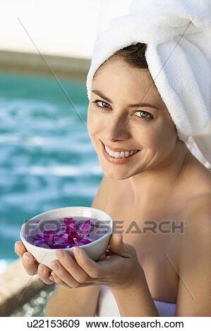 Stock Photo - Caucasian mid-adult woman wearing towel around head and body holding bowl of purple orchids next to pool.. Fotosearch