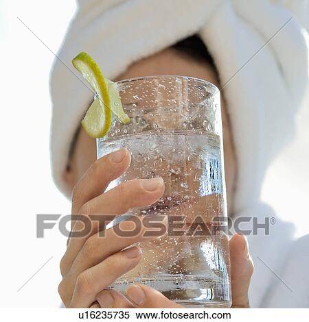 Stock Photography - Caucasian mid-adult woman with towel on head holding drink glass with lime slice in front of face.. Fotosearch