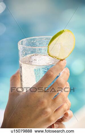 Woman's hands holding drink glass garnished with lime slice next to pool View Large Photo Image Stock Photo - Woman's hands holding drink glass garnished with lime slice next to pool. Fotosearch