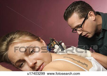 Stock Photo - Caucasian male tattoo artist tattooing Caucasian woman.. Fotosearch
