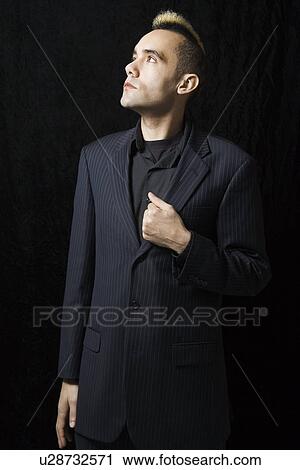 Stock Image - Caucasian man in suit with mohawk standing posed against black background.. Fotosearch